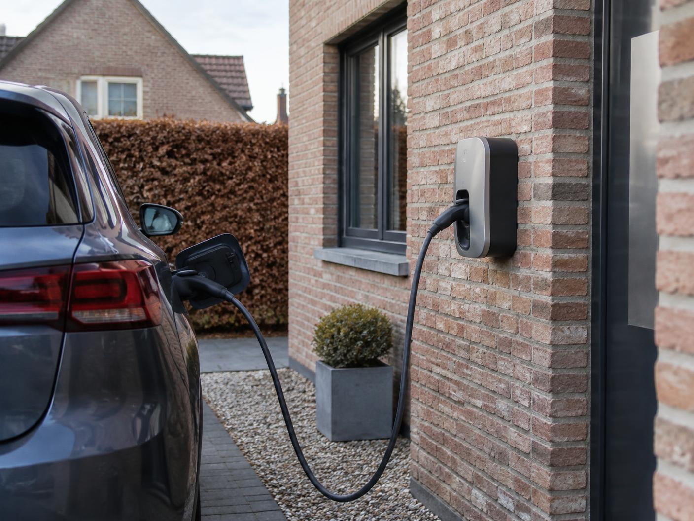 Residentiële laadpaal aan een bakstenen woning met een wagen op de oprit.